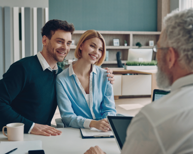 Two people smiling in a meeting across a desk from an older man in an office setting