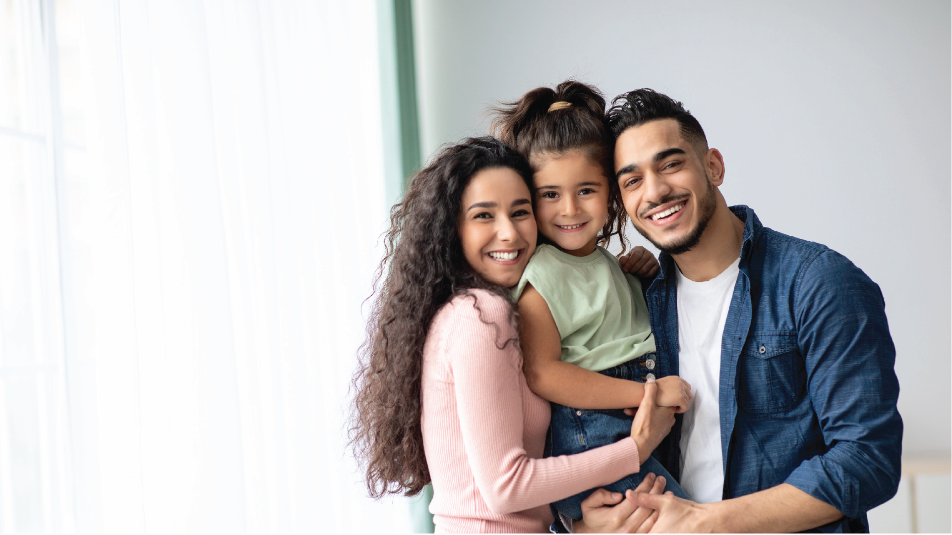 A smiling family of three posing for a photo against a light background.