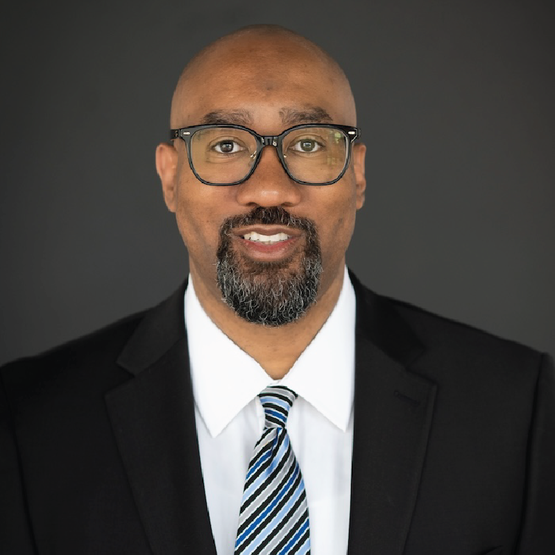 A man in a suit shakes hands with another man in a blue shirt
