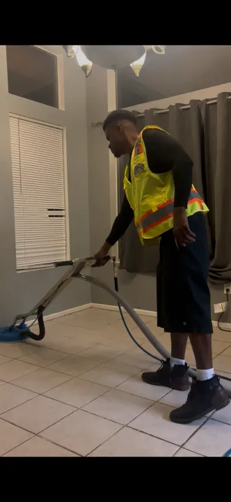 Electrician working on a circuit breaker panel. He wears a hat and coveralls, indoors.
