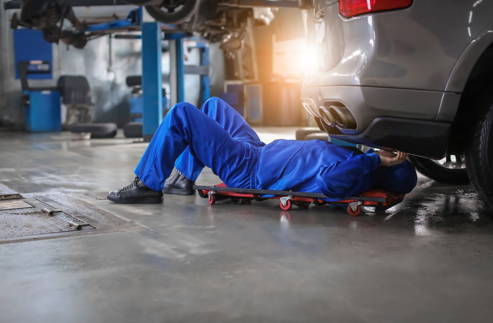 Mechanic lying under a car in a garage, working on the underside with tools nearby.
