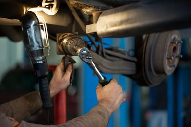 Mechanic tightening a pipe fitting under a vehicle with a wrench in a garage
