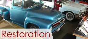 Classic blue pickup and white car in a garage with “Restoration” text