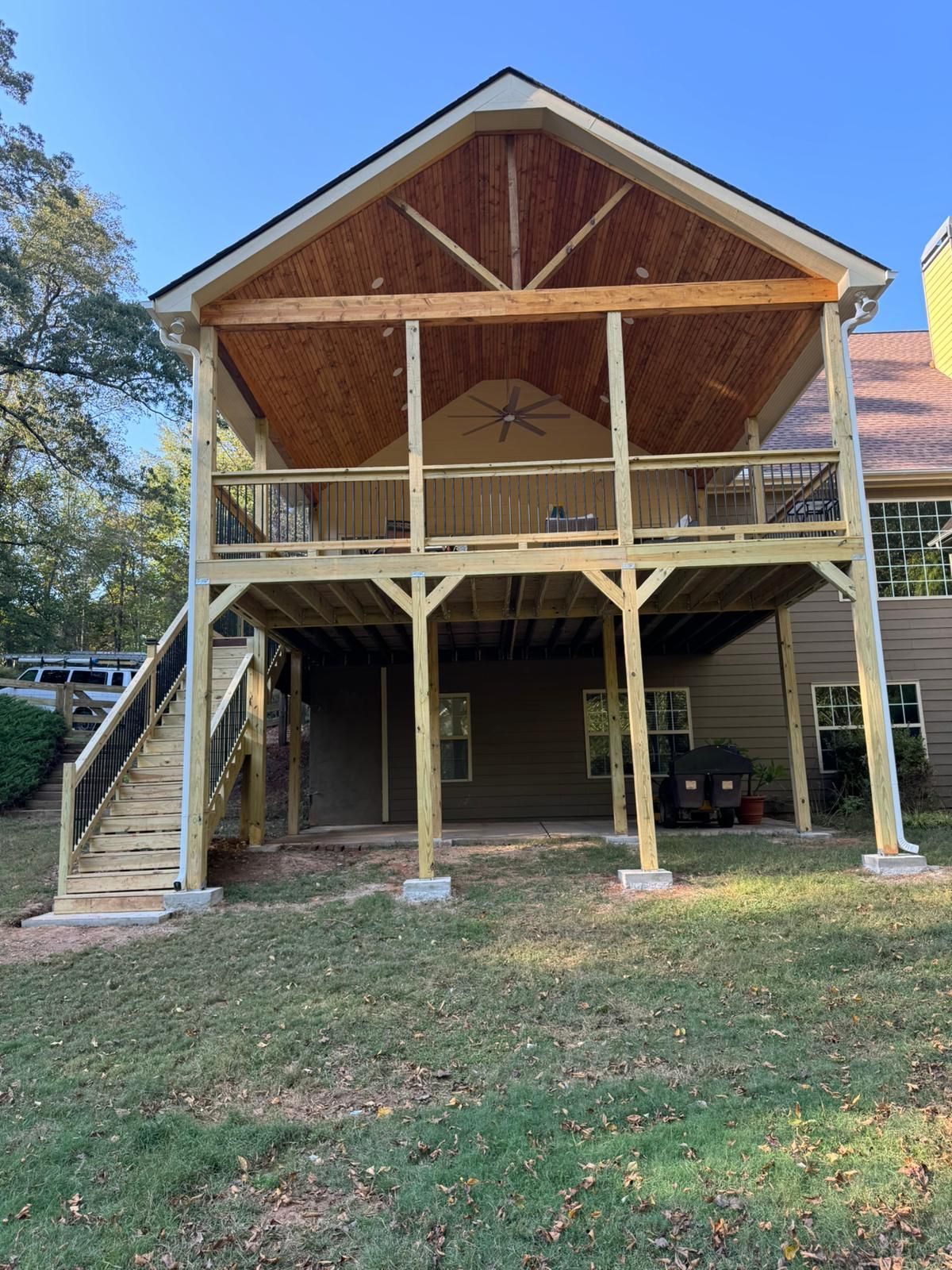 Two-story wooden deck with a covered upper level. Brown ceiling, light wood structure, concrete pillars, and steps.