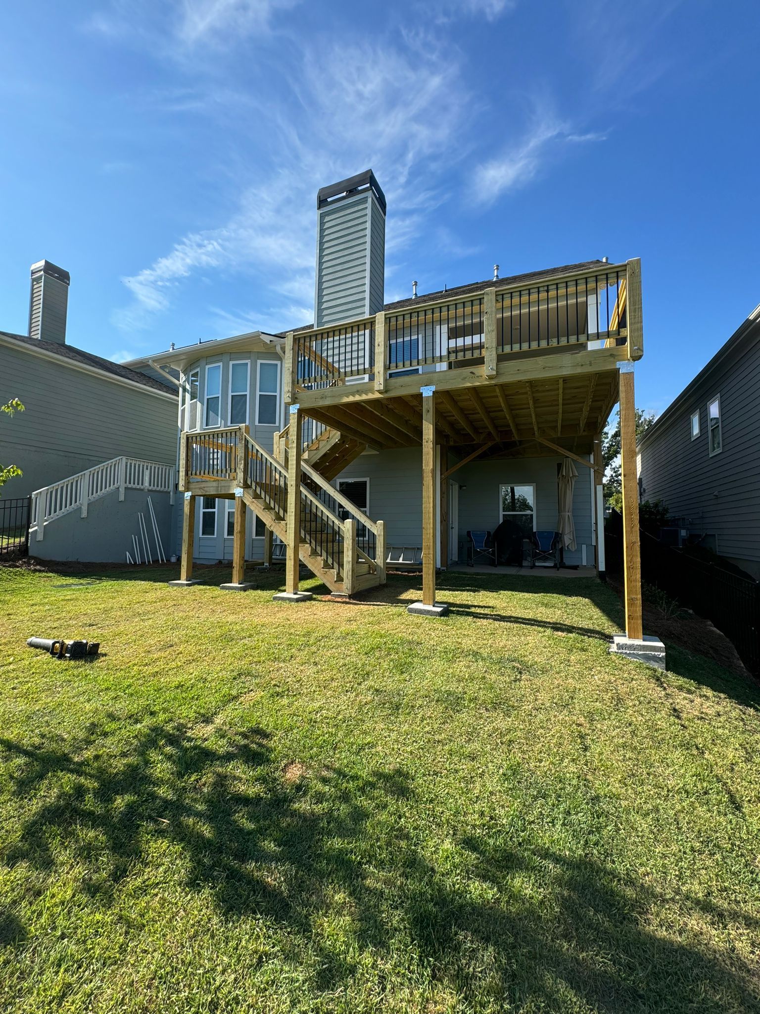 Backyard with new wooden deck attached to a gray house under a blue sky.