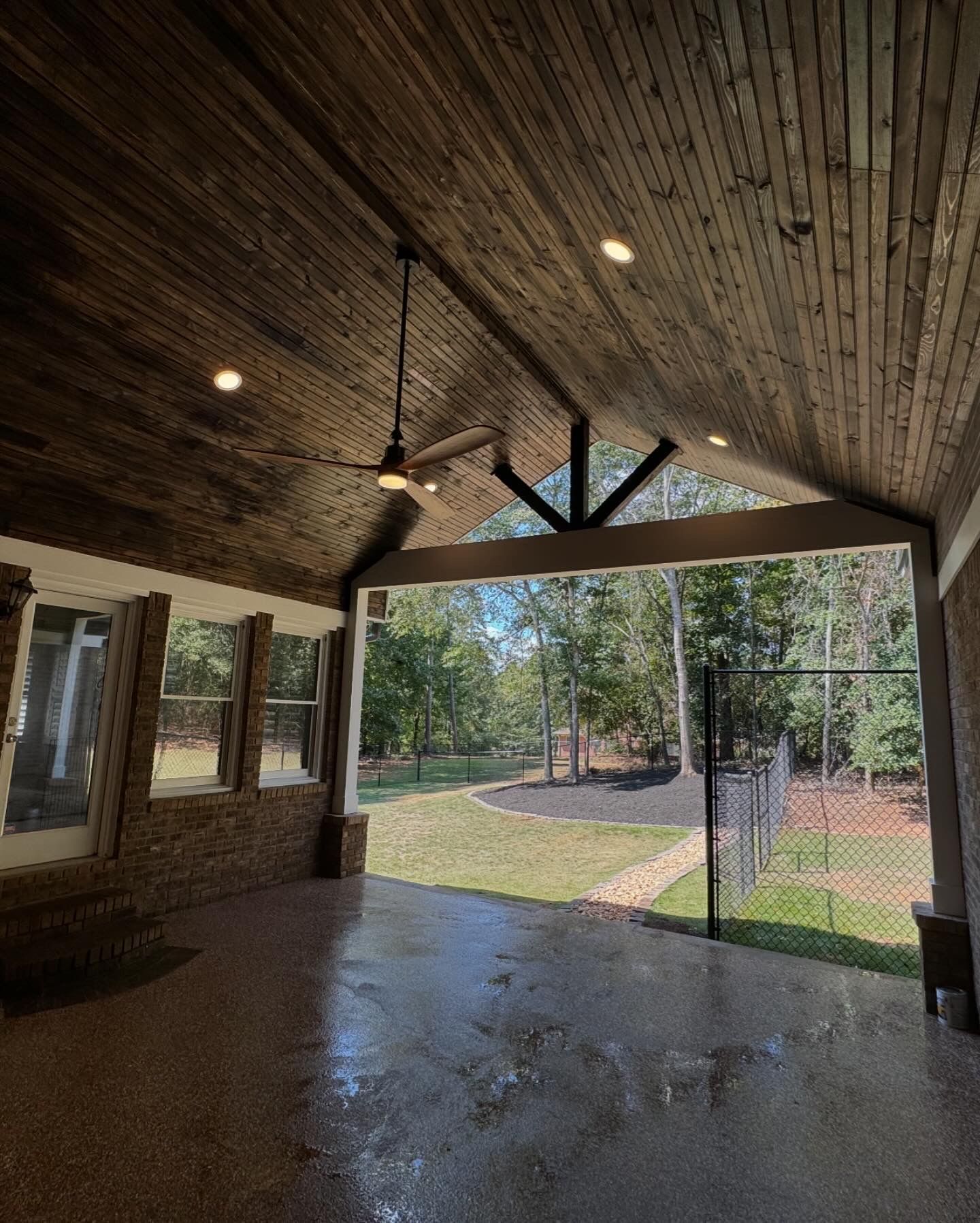 Covered patio with wood ceiling and a view of a grassy yard, trees and a fence.