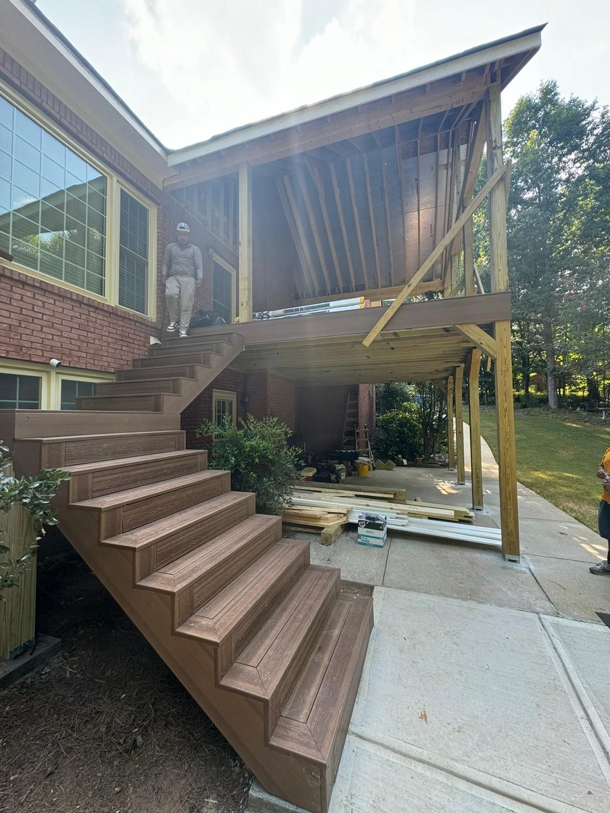 Deck stairs leading to a partially constructed covered deck attached to a brick house. A person stands on the stairs.