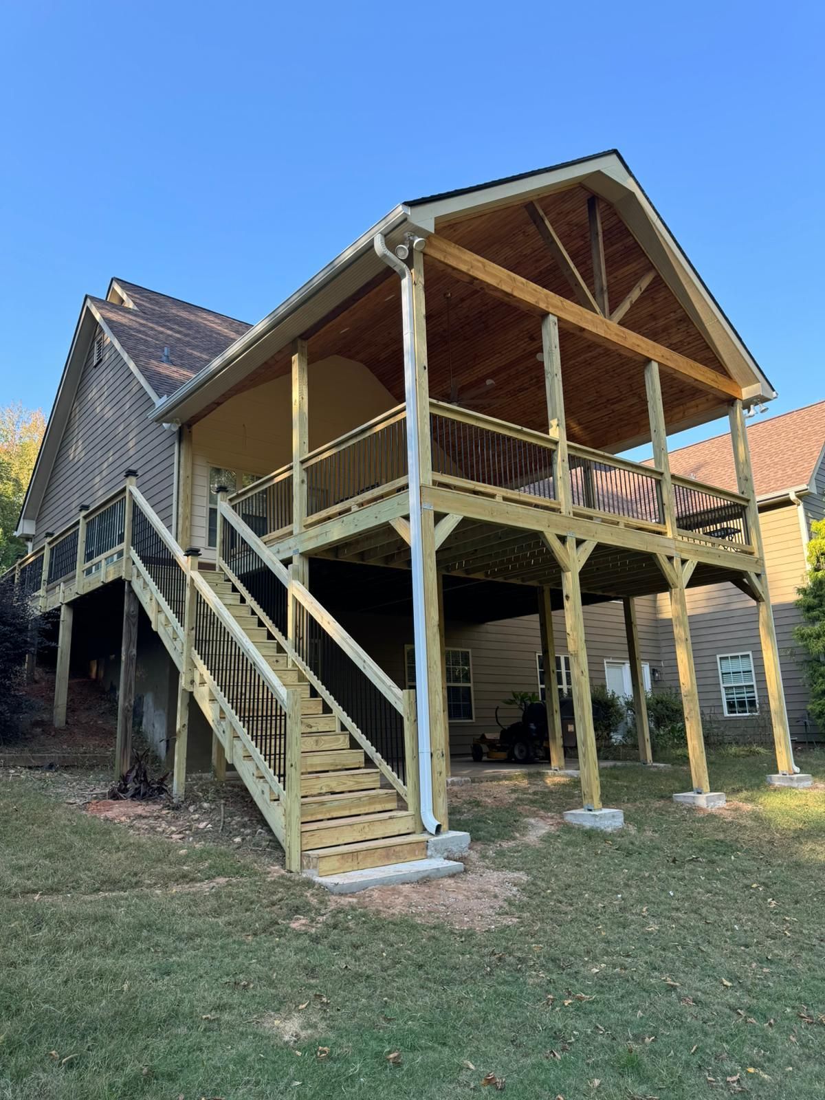 Two-story wooden deck with stairs attached to a house with a clear blue sky in the background.
