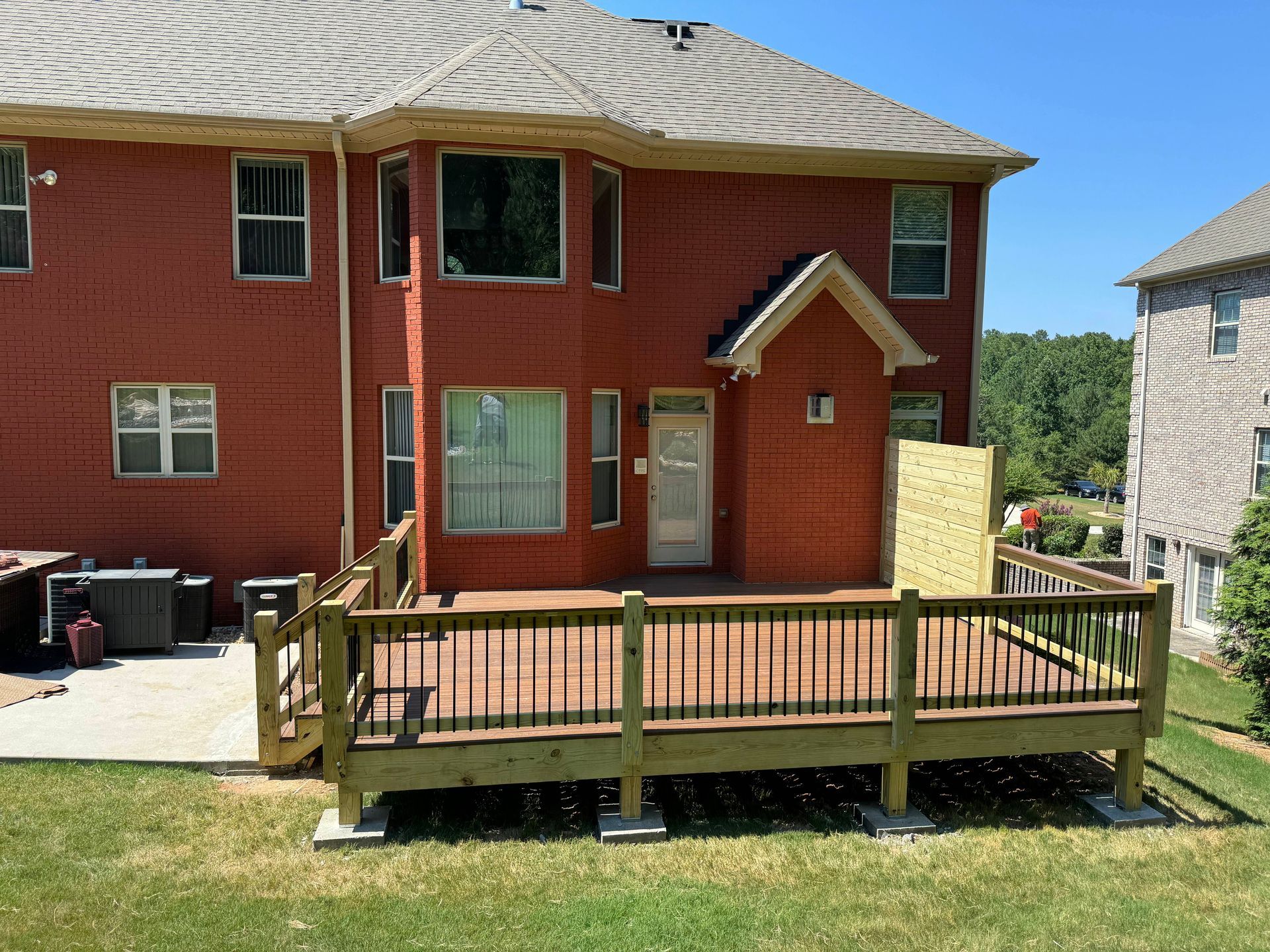 Backyard deck with railing, connected to a red brick house; plywood leans against the house.