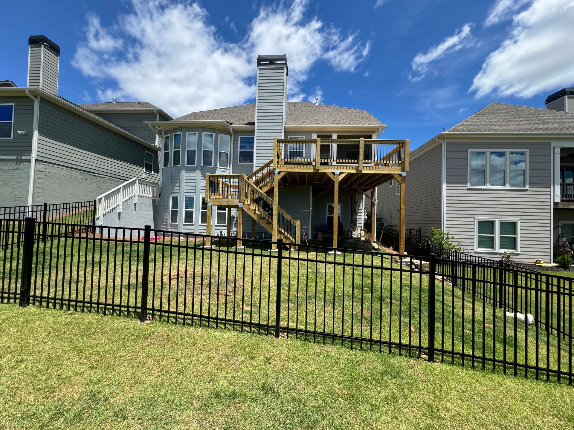 Rear view of a light blue two-story house with a wooden deck. The house has a black fence and chimney.