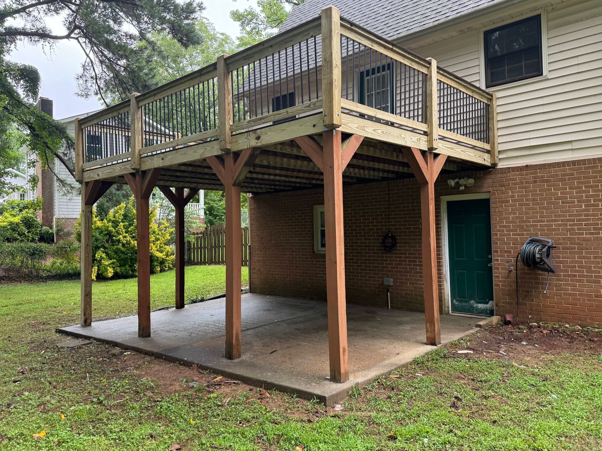 Wooden deck over a concrete patio; attached to a brick house, supported by wooden posts.