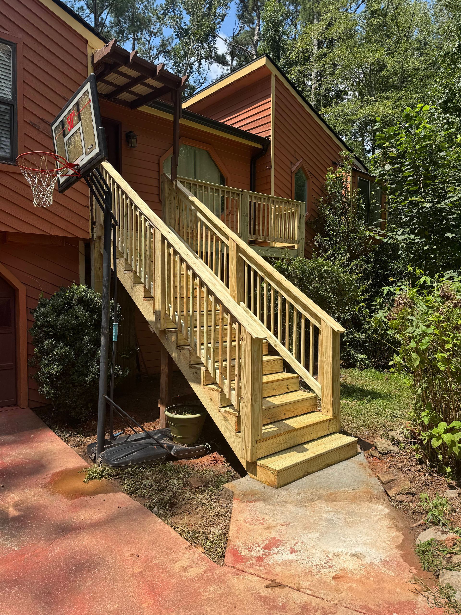 Wooden outdoor staircase leading to a house entrance; basketball hoop at the bottom.