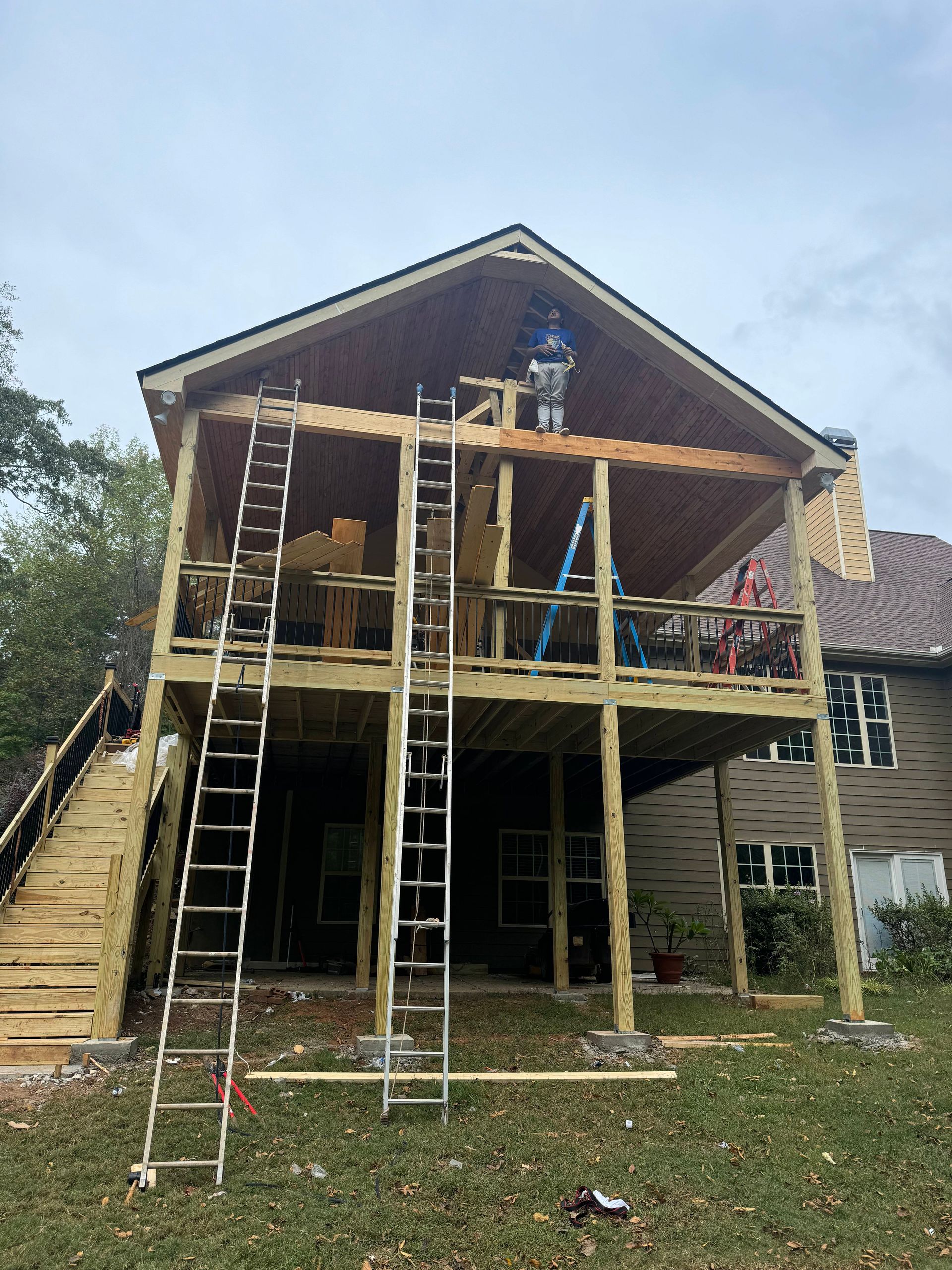 Two-story wooden deck addition under construction on the back of a house; ladders present.