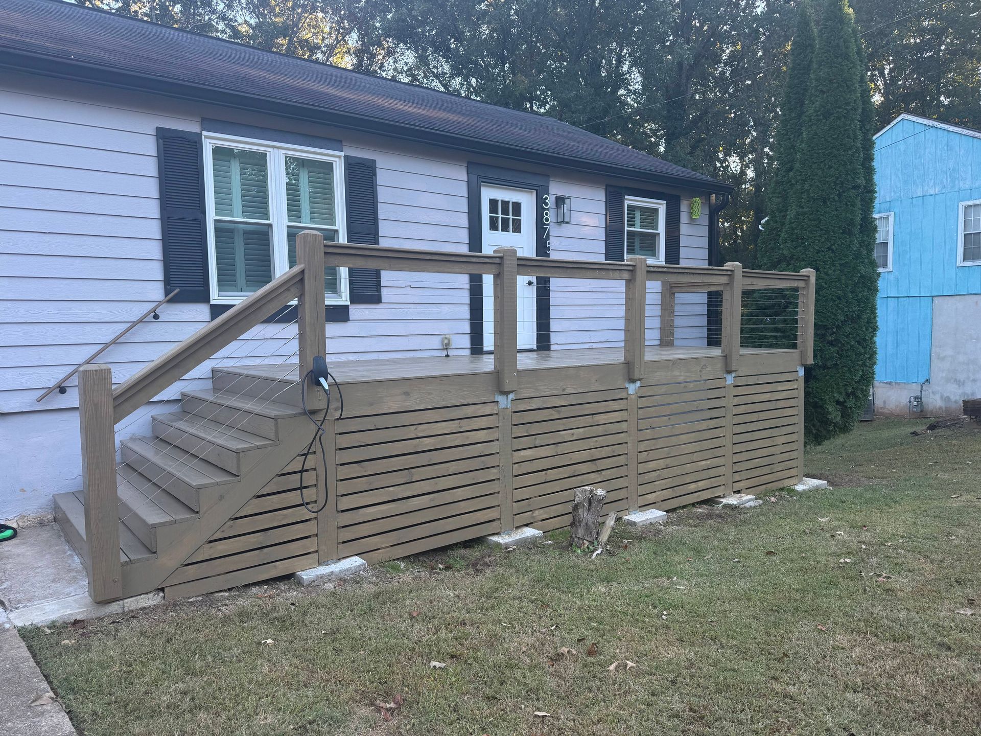 A light gray house with a wooden deck and stairs. The deck has horizontal slats for privacy.