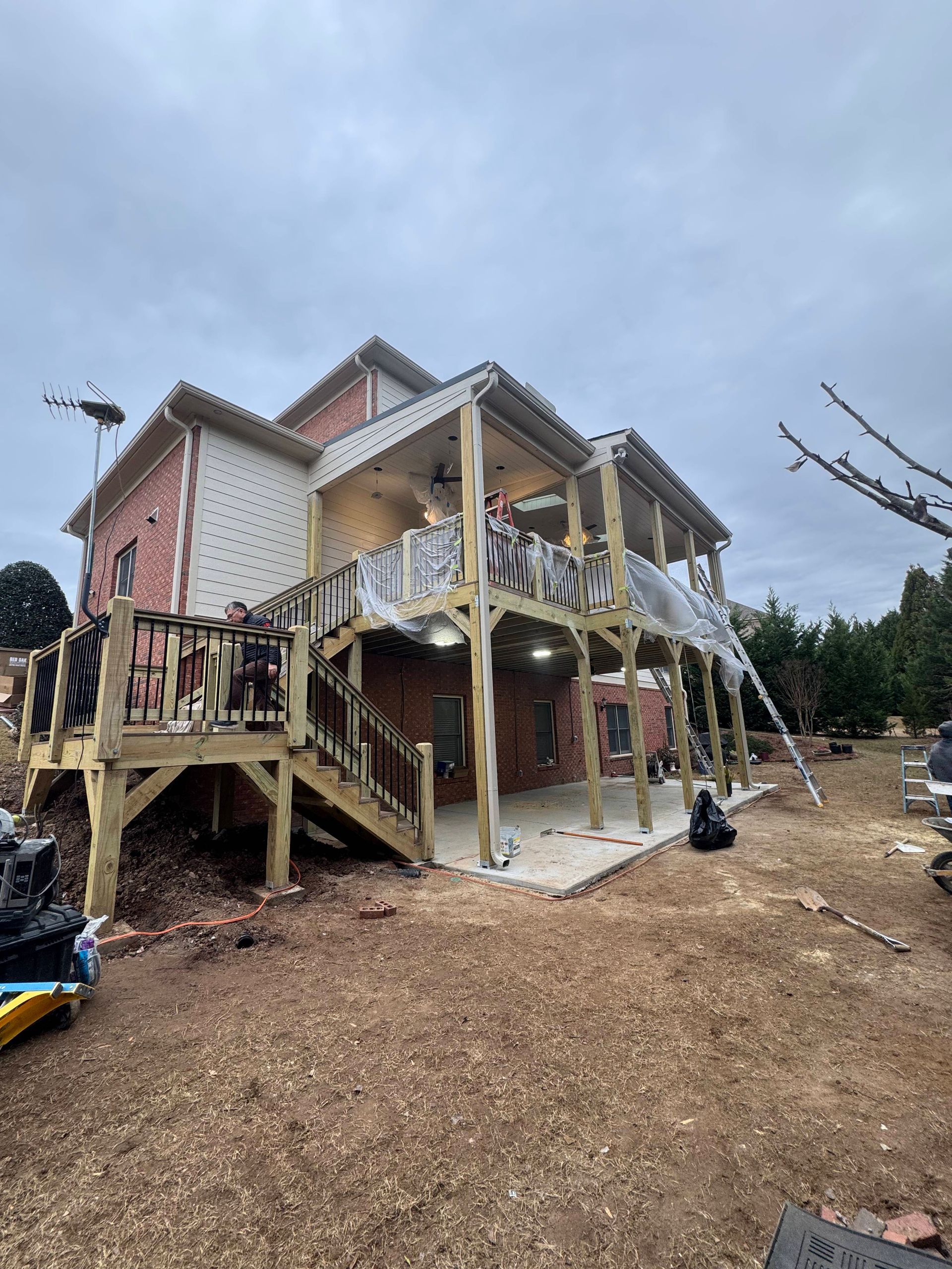 Wooden deck under construction on a two-story brick house, with a cloudy sky.