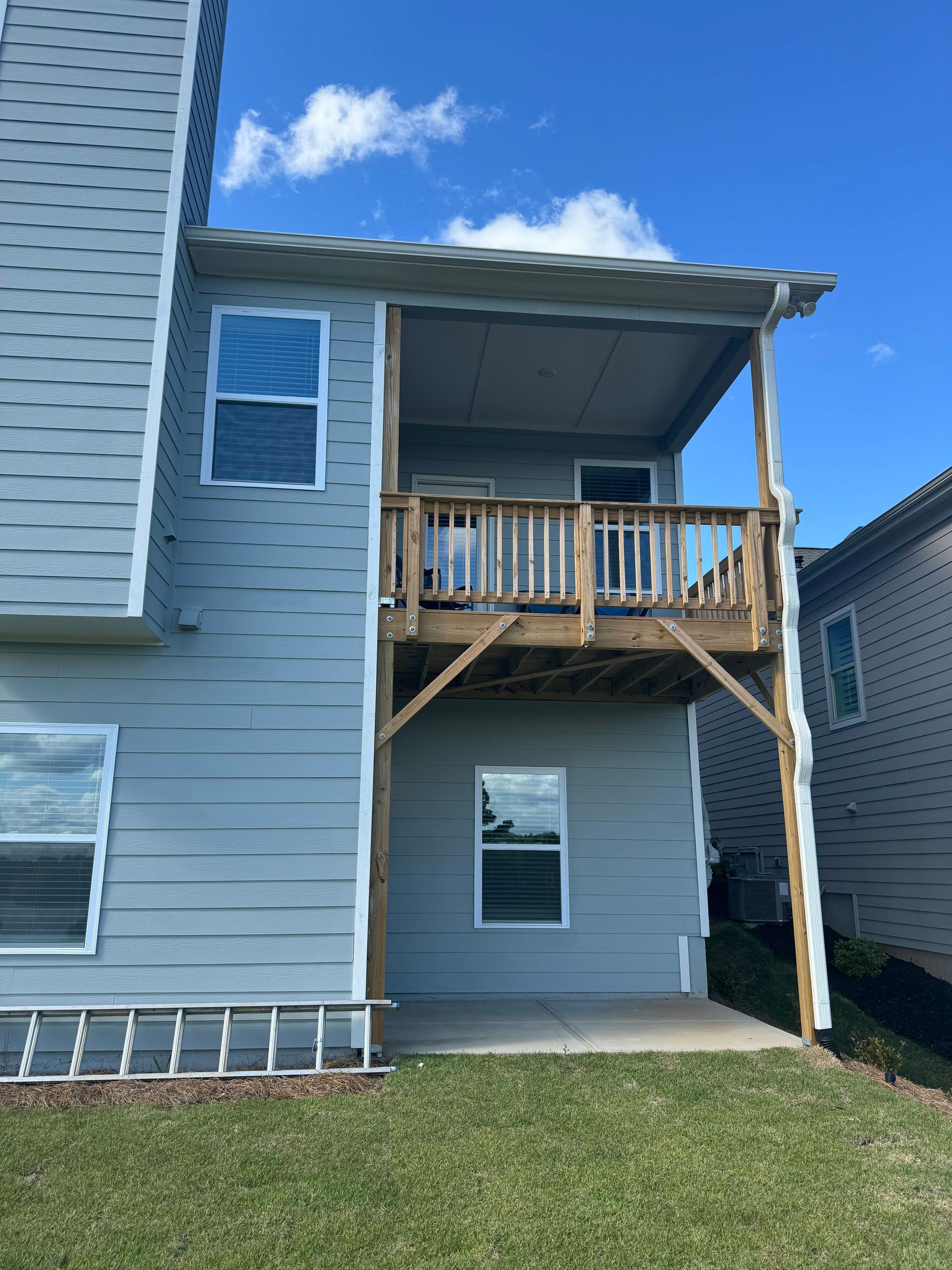 Backyard with a two-story deck, gray siding, chimney, and blue sky.