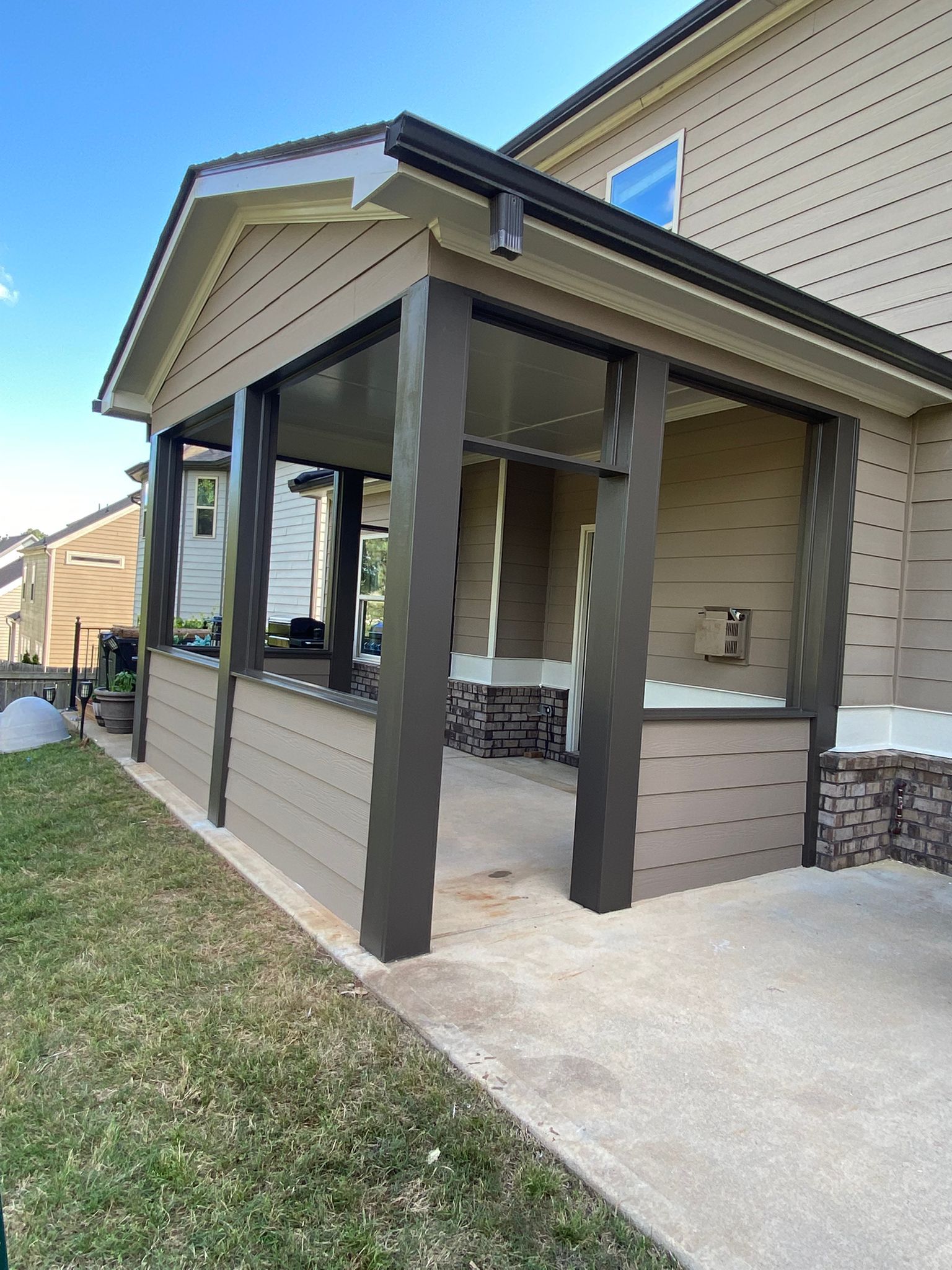 Covered porch with brown columns, tan siding, concrete path, and green grass.
