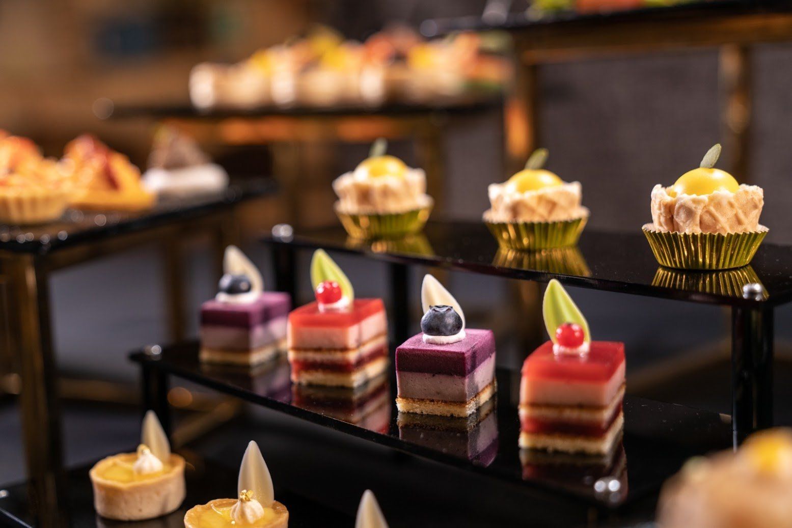 甜點展示：分層蛋糕、蛋塔和紙杯蛋糕，放在分層的黑色托盤上；自助餐設定。
