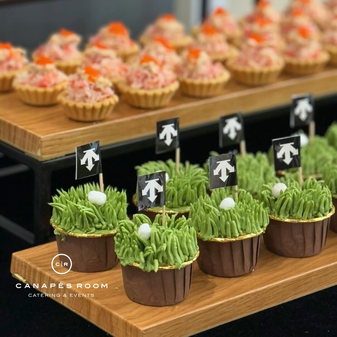 開胃菜展示：迷你乳蛋餅配海鮮和草糖霜紙杯蛋糕配高爾夫球糖和旗幟。