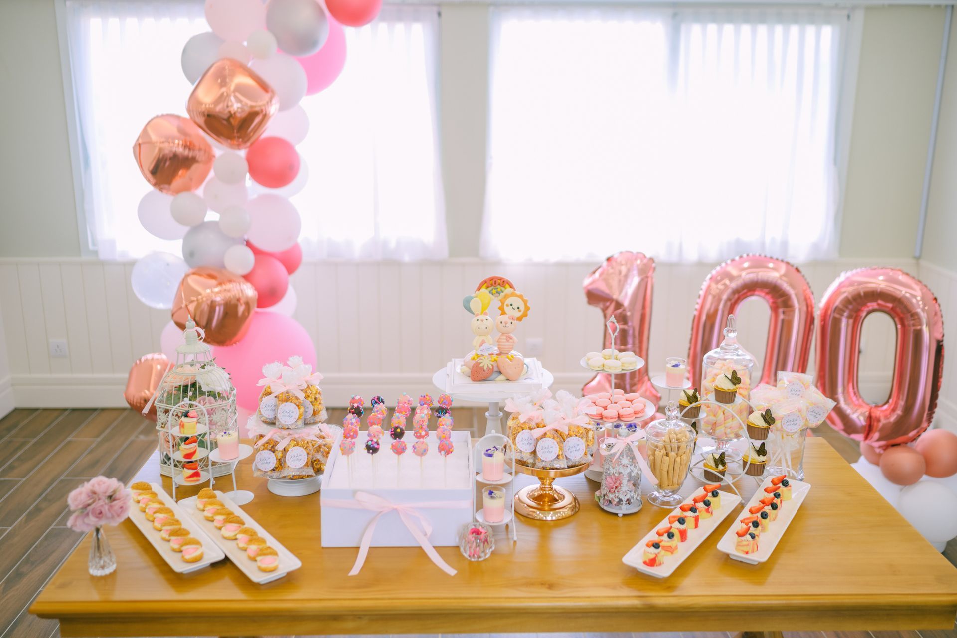 Dessert table for a 100th birthday with balloons in pink, white, and rose gold.