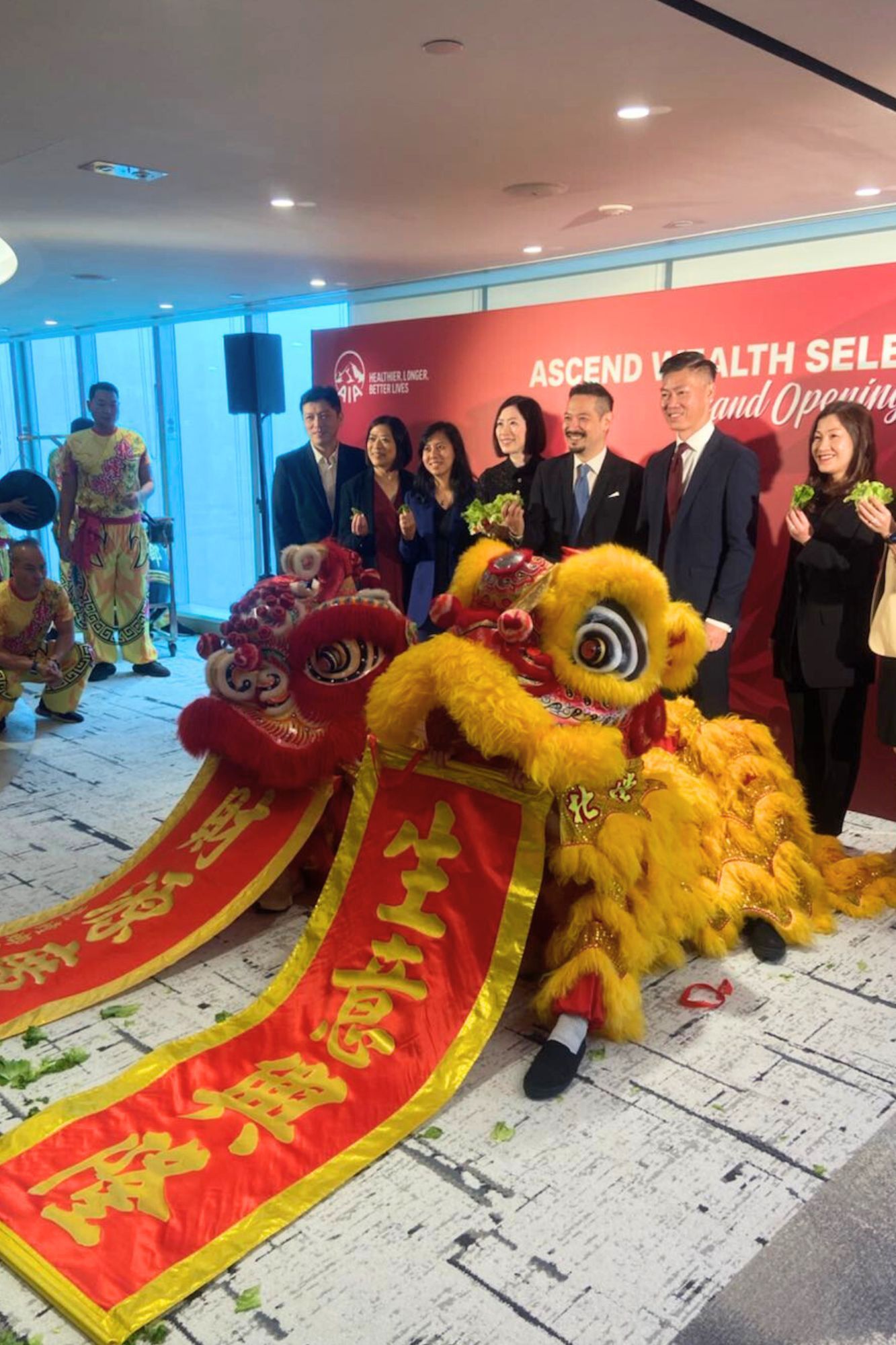 慶祝活動中,人們身著西裝,手拿紅色橫幅,周圍飄揚著五彩紙屑,舞獅。