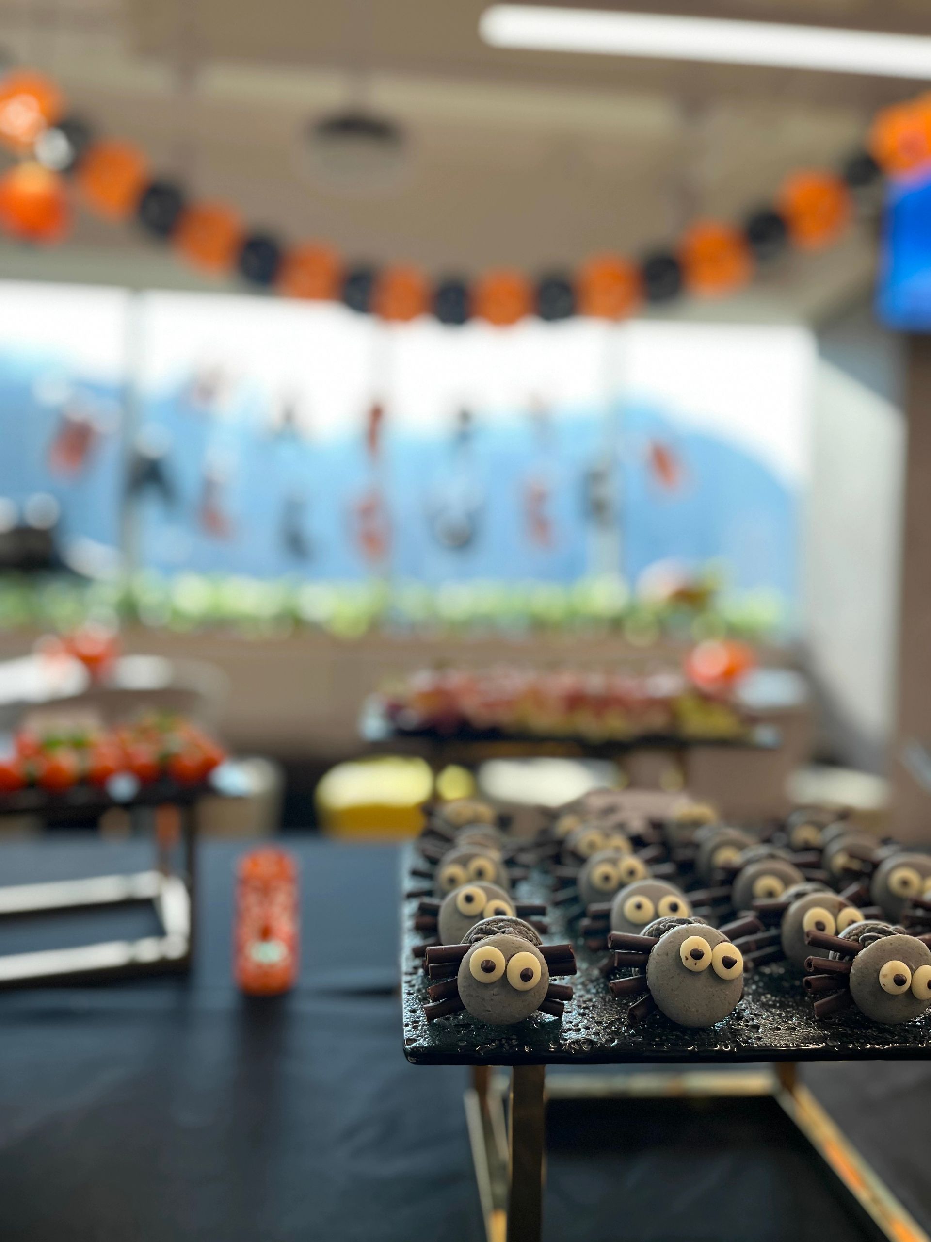 Halloween-themed dessert table with spider cake pops, orange and black decorations, in front of a window.