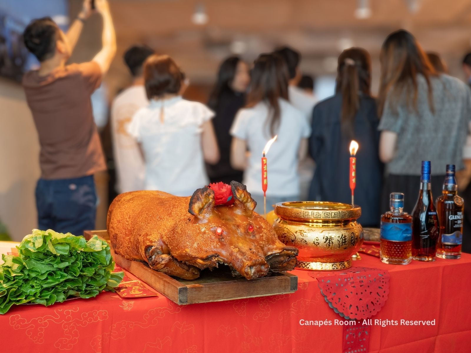 桌上有烤豬,點著蠟燭和酒,背景有人。