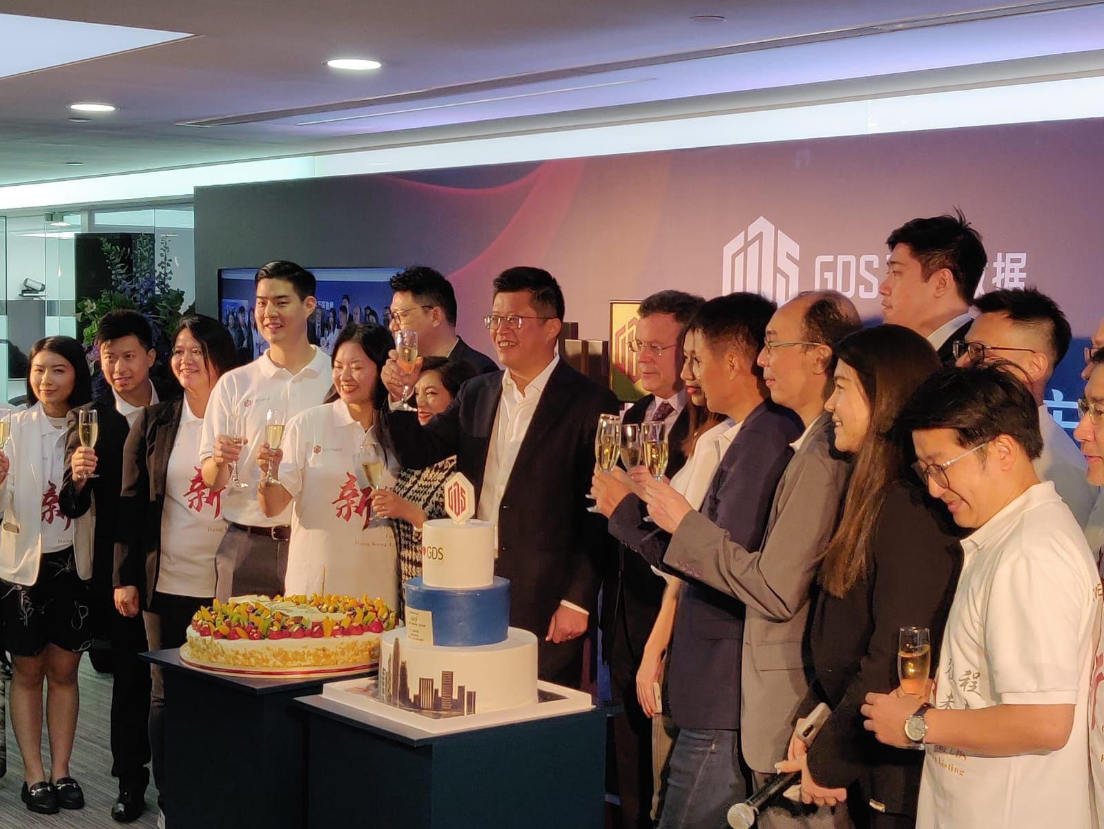 Group celebrates with cake and champagne, likely at a company event.