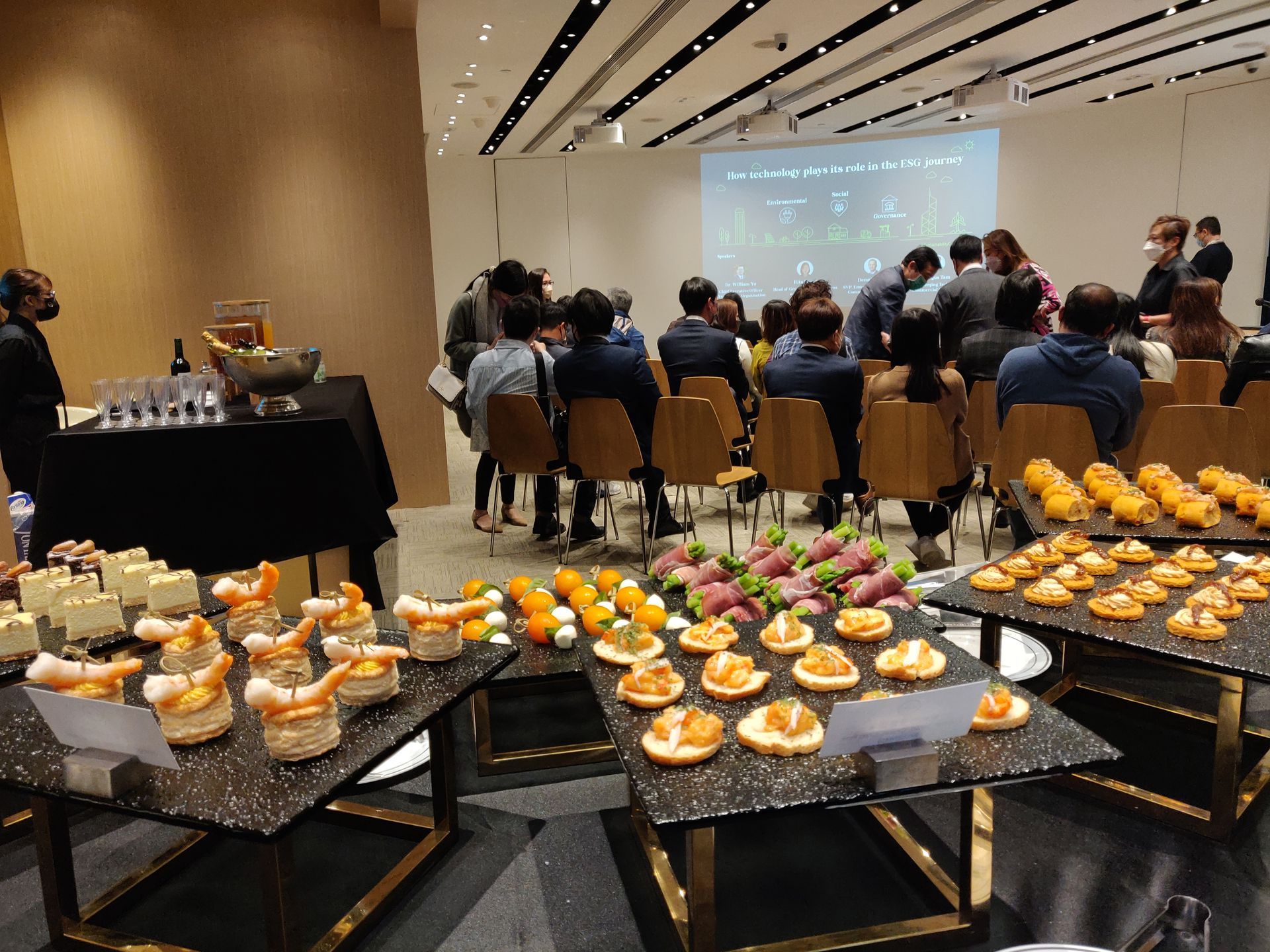 Buffet spread with seated audience watching a presentation on a screen in a modern room.