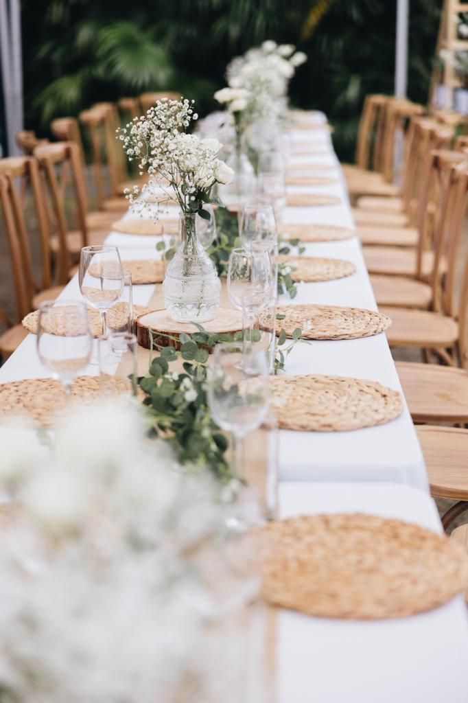 Long table set for an event with white tablecloth, floral centerpieces, and place settings.