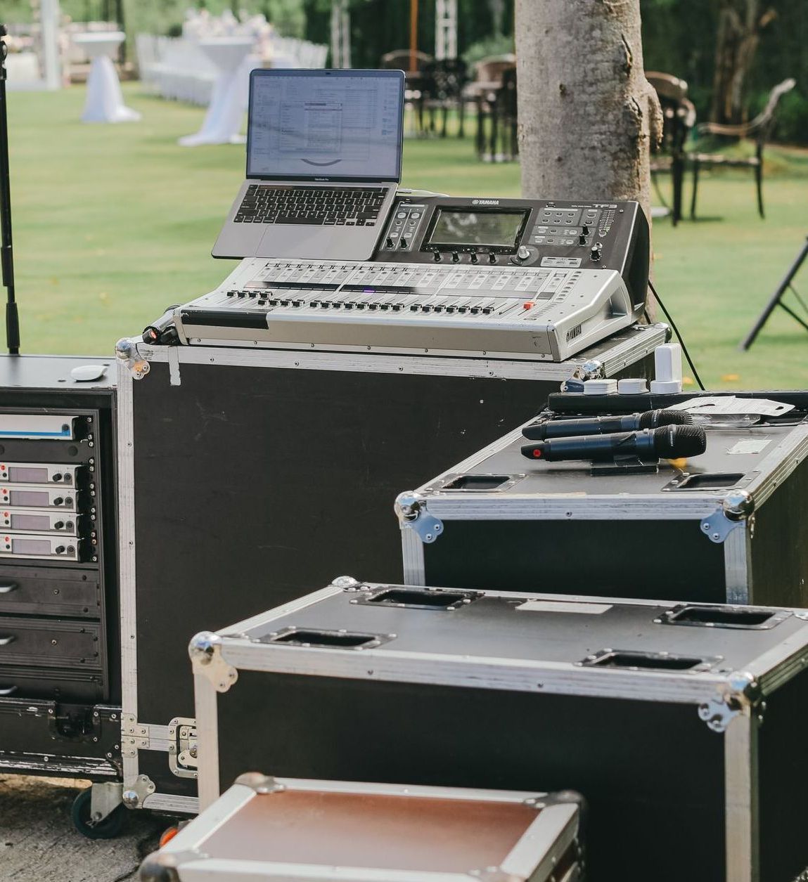 Audio equipment setup outdoors on a grassy area, including a laptop, mixer, and microphones.
