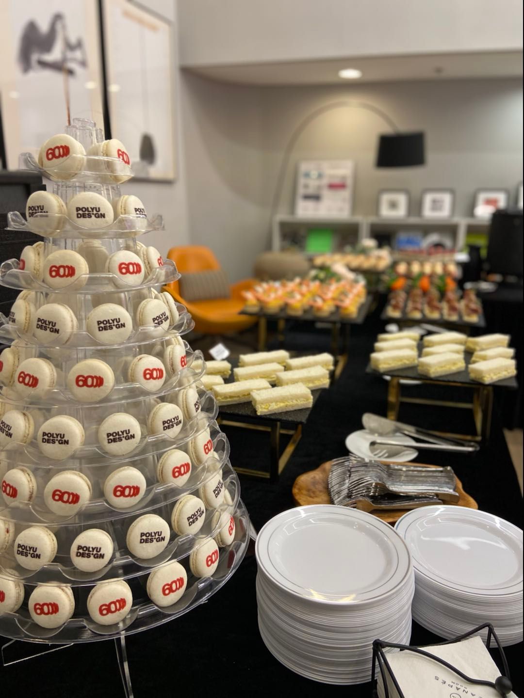 甜點桌：擺放著開胃菜的馬卡龍塔，盤子疊放整齊。室內活動，背景為藝術品。