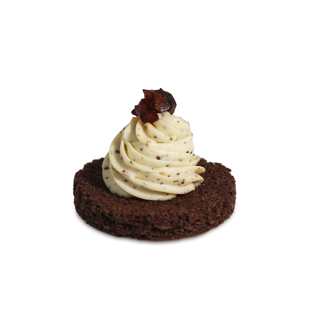 Small chocolate cake topped with swirled cream and a dark garnish.