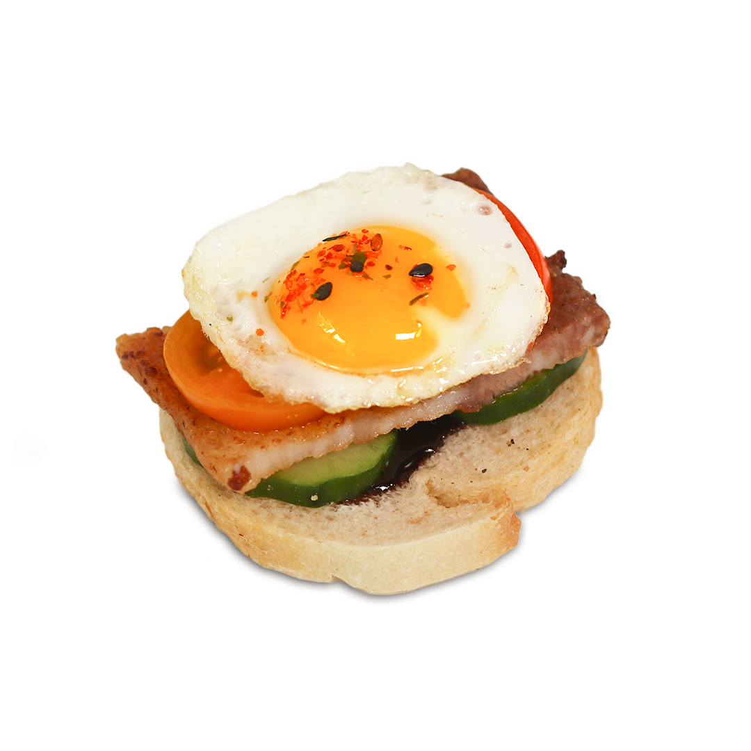 Mini breakfast sandwich: bread base with cucumber, tomato, bacon, and a fried egg with paprika.