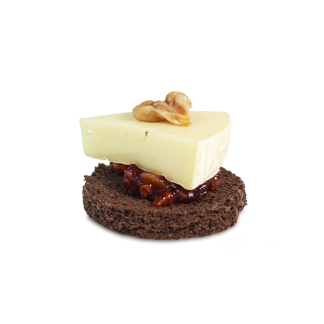 Appetizer: cheese wedge with walnut on top of a dark bread round with chutney.