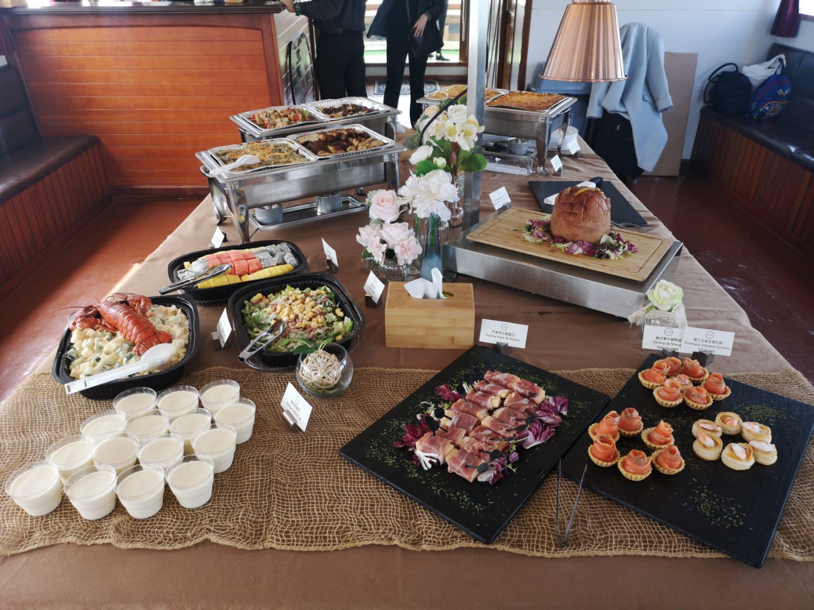 Buffet table with various dishes, including meat, salads, and appetizers. Beige tablecloth, wooden interior.