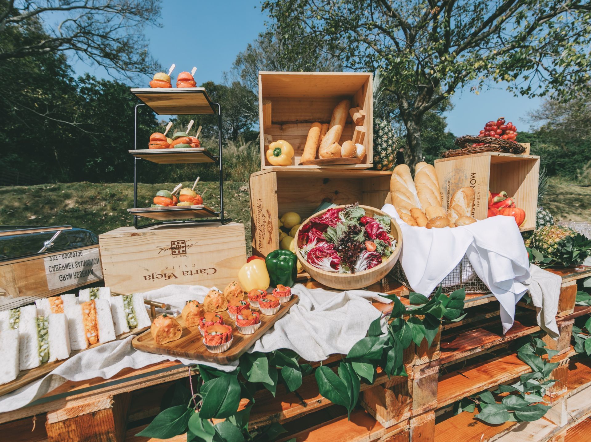 Outdoor food display with bread, sandwiches, and small appetizers on wooden crates and pallets.