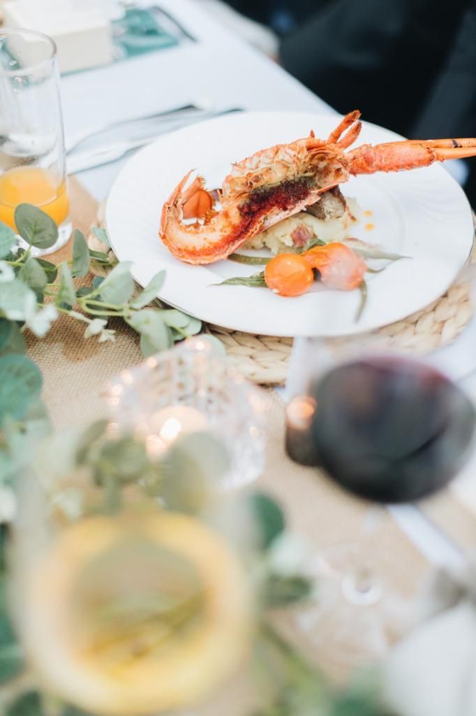 Lobster dish on a white plate, served on a decorated table with greenery and candles.