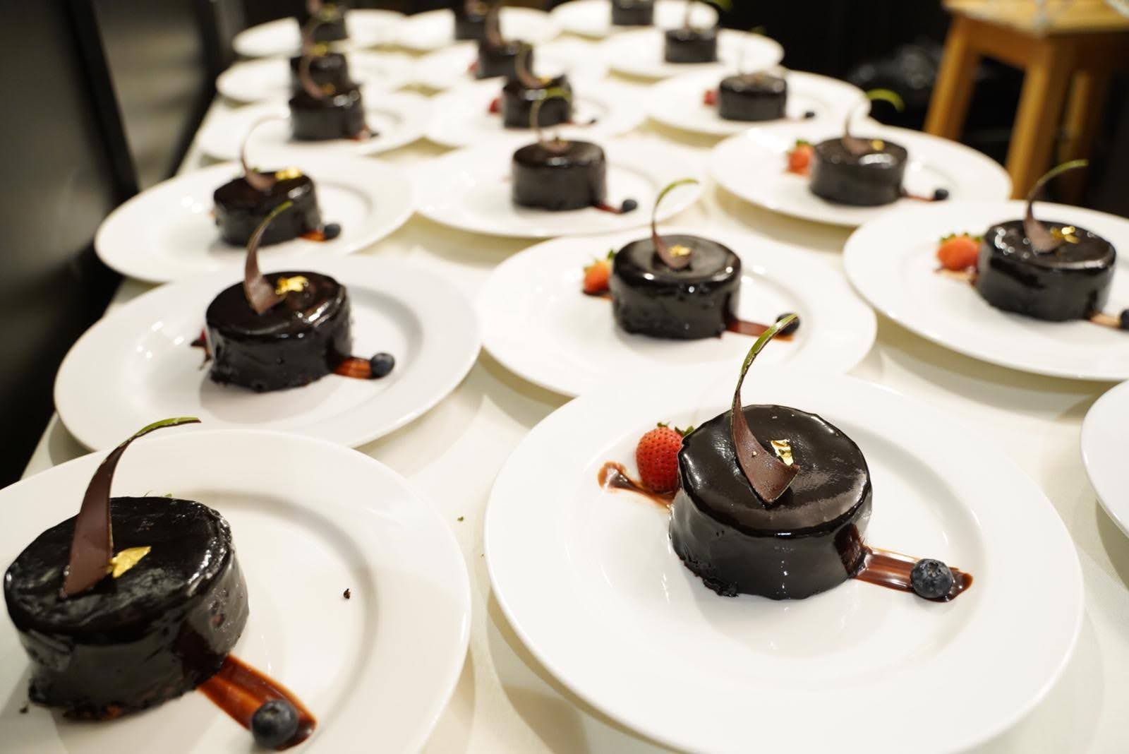Plated chocolate desserts with berries and gold accents, arranged on a white table.