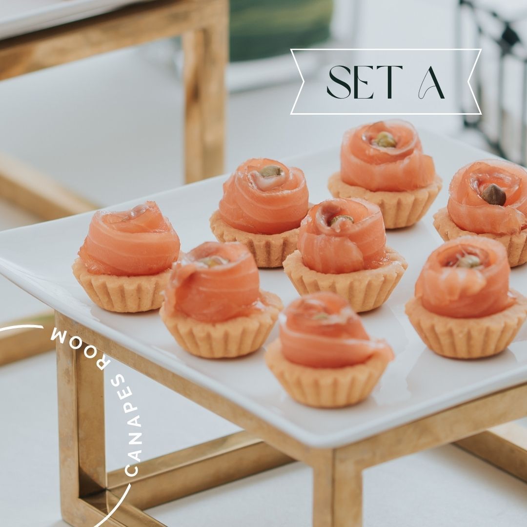 配有鮭魚玫瑰的開胃小菜盛放在糕點杯中，放在帶有金色支架的白色方形盤子上。