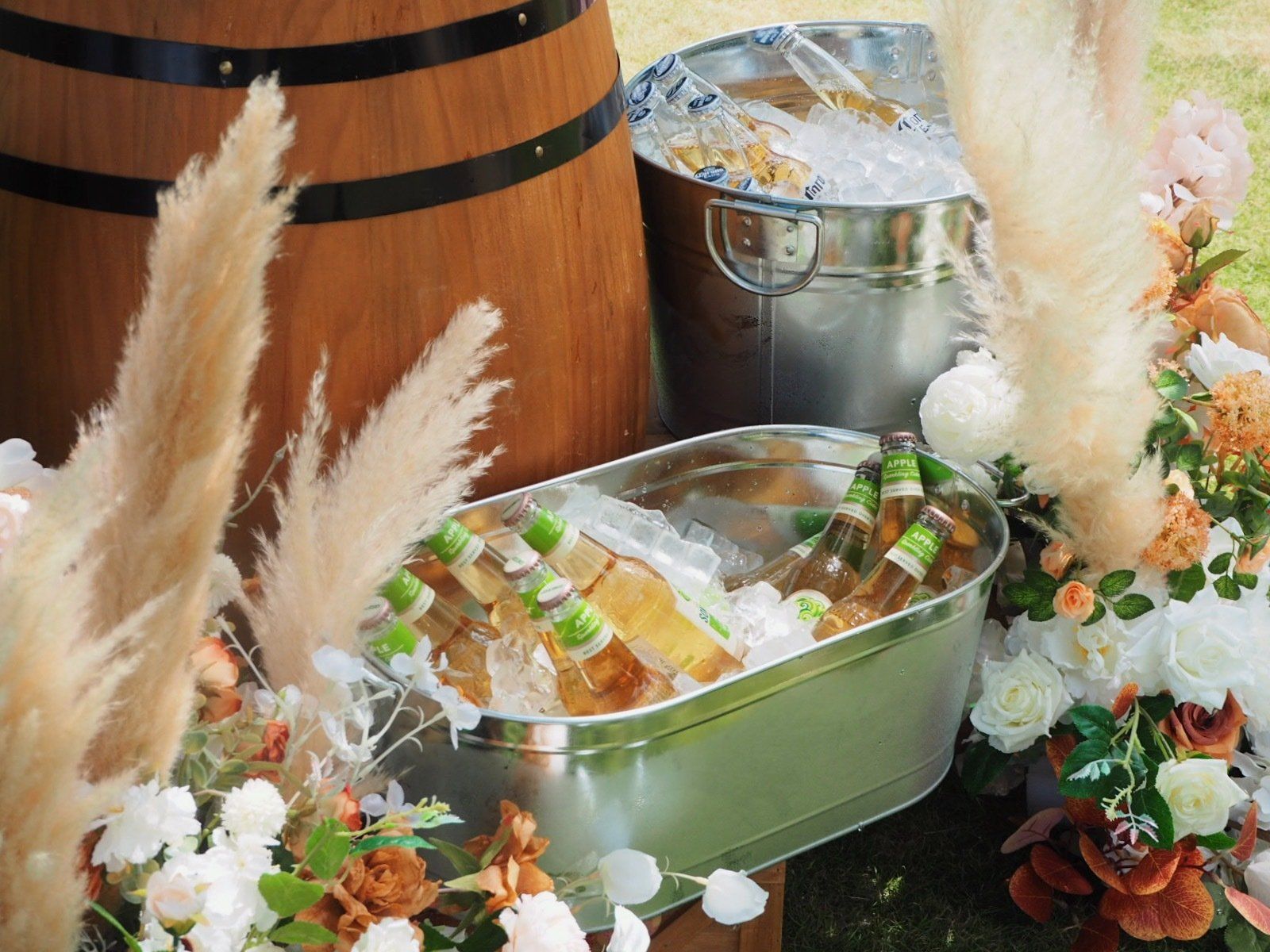 Beer in metal tubs with ice, next to a wooden barrel and floral decorations.