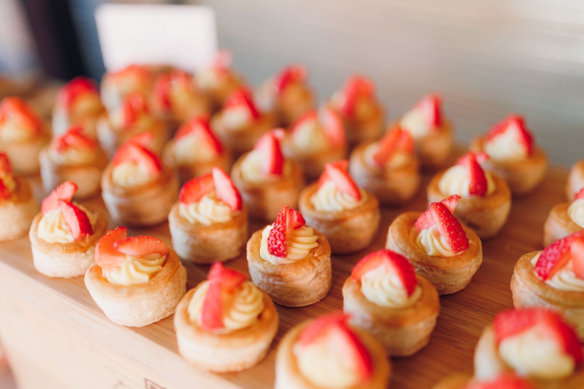 Mini strawberry tarts with creamy filling on a wooden serving board.