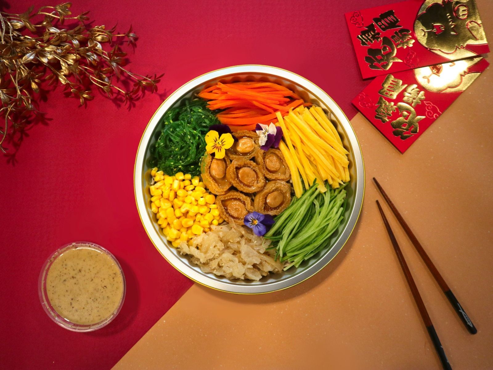 Colorful Chinese New Year salad with abalone, vegetables, and sauce, arranged on a red and gold surface.
