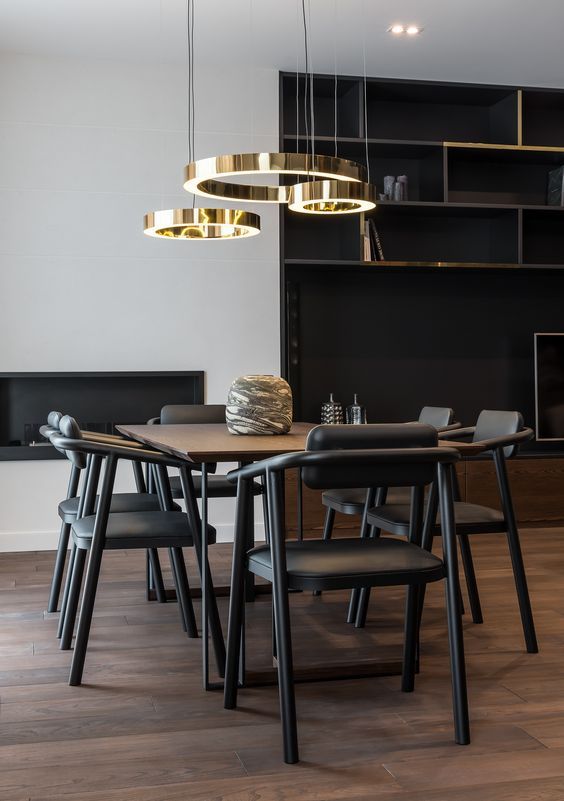 Dining room with dark wooden table, black chairs, gold pendant lights, and built-in shelving.