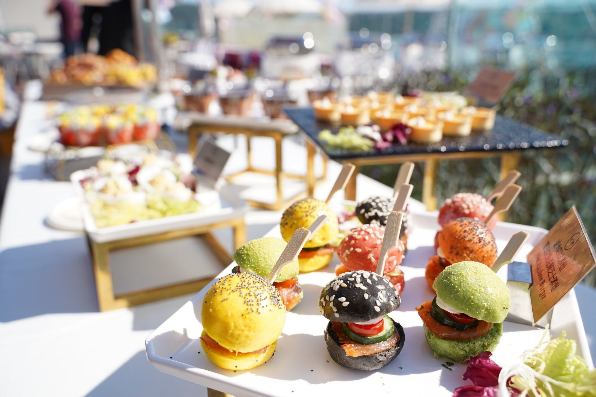 Buffet with colorful mini burgers, salads, and appetizers on a bright outdoor table.
