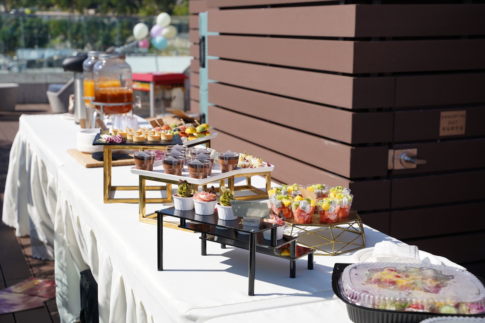 Buffet table with cupcakes, drinks, and snacks set outdoors.