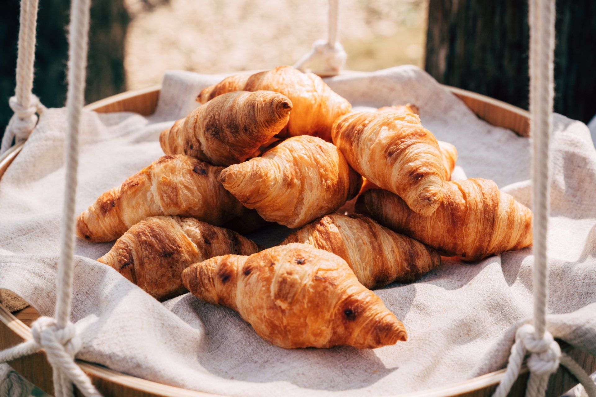 Golden croissants piled in a wooden tray lined with a light linen cloth.