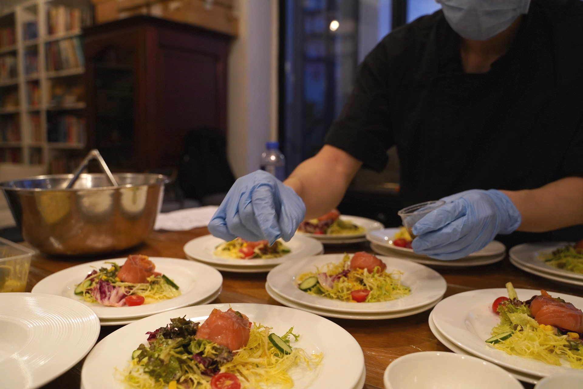 Chef in blue gloves garnishes plated salads with yellow vegetables.