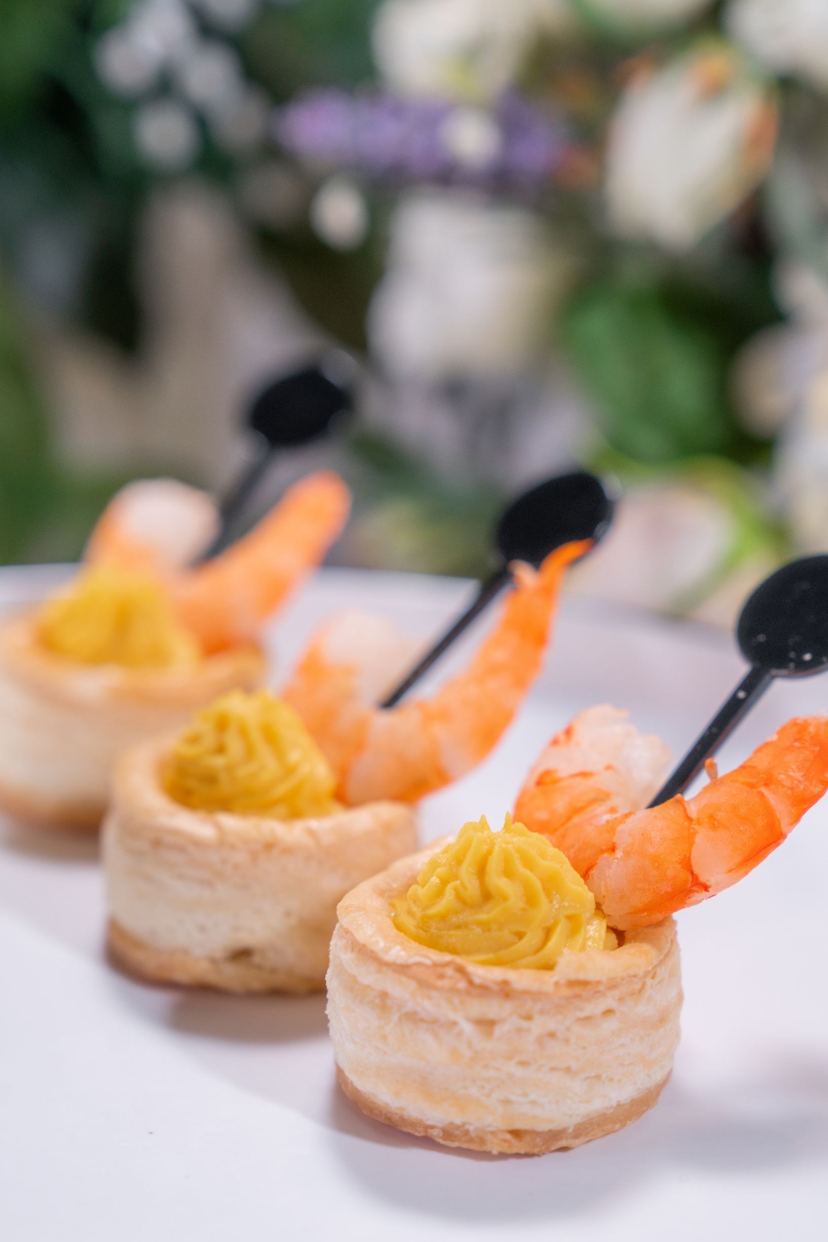 Shrimp hors d'oeuvres: Puff pastry shells with yellow filling and shrimp, skewered with black picks.