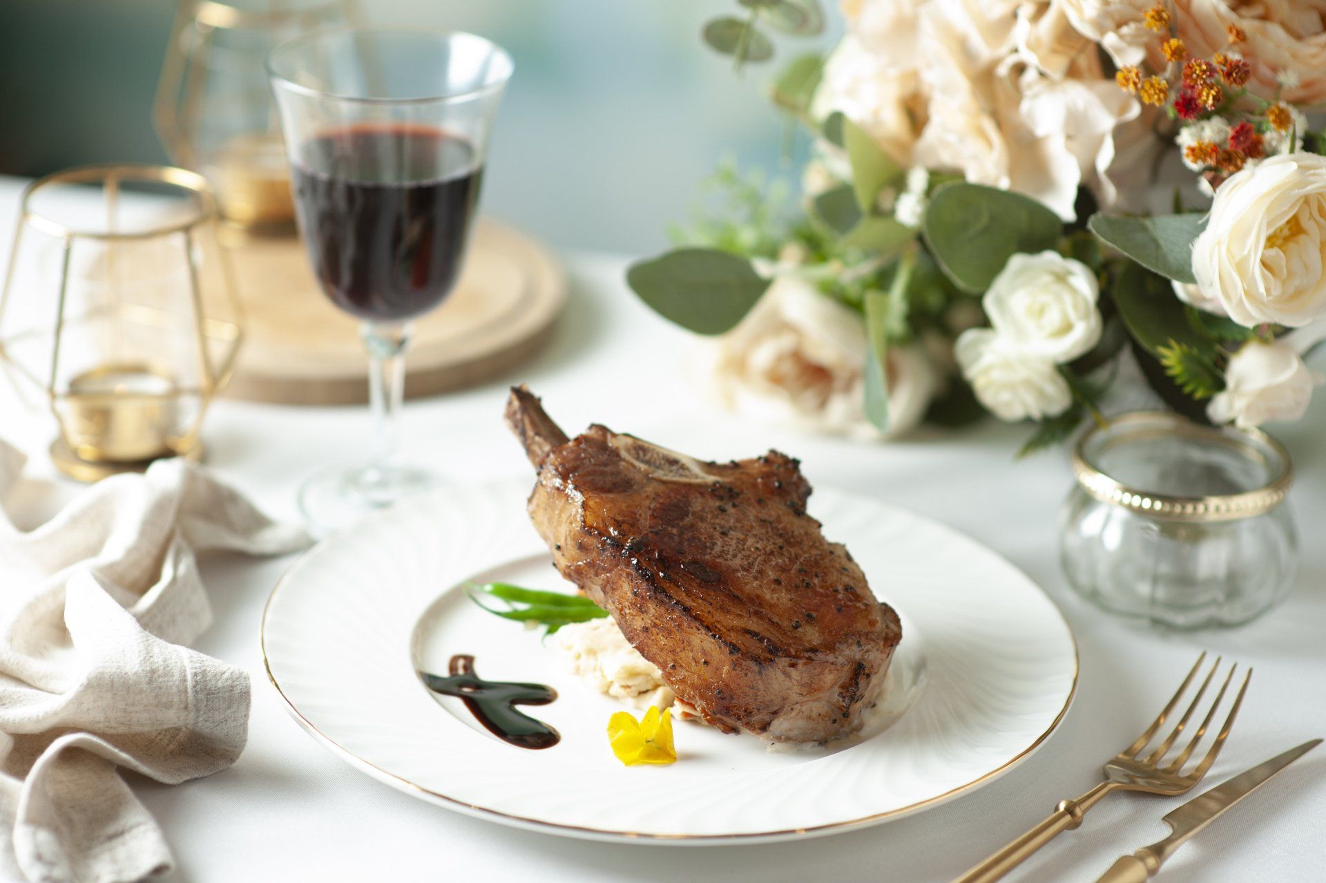 Steak dinner on a white plate with red wine, flowers, and gold accents.